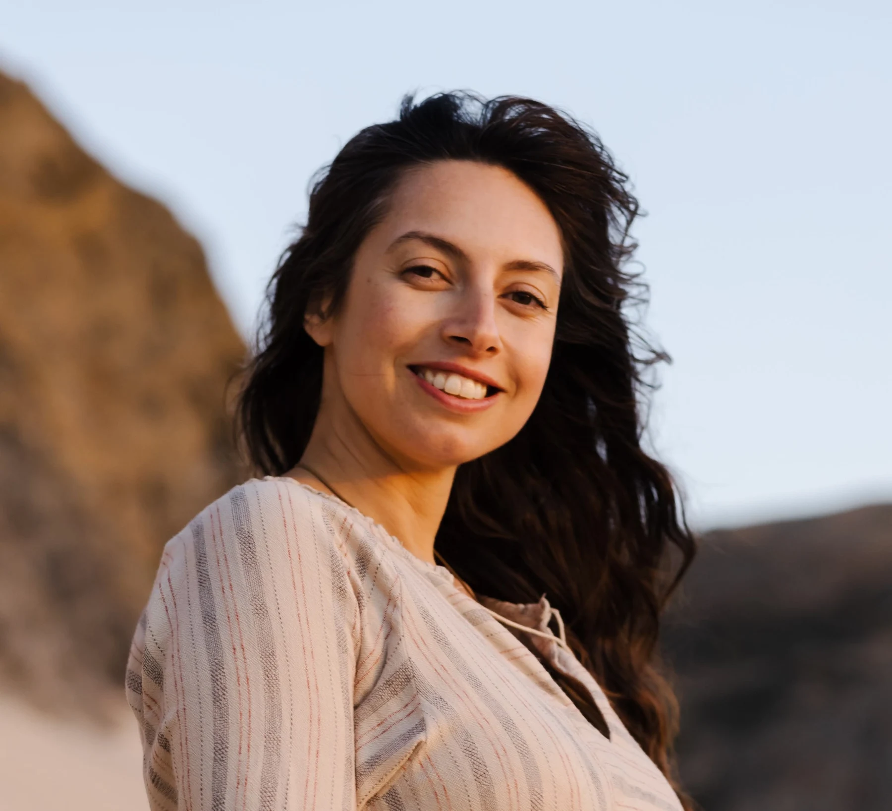Emi smiling in warm evening light by the coast.
